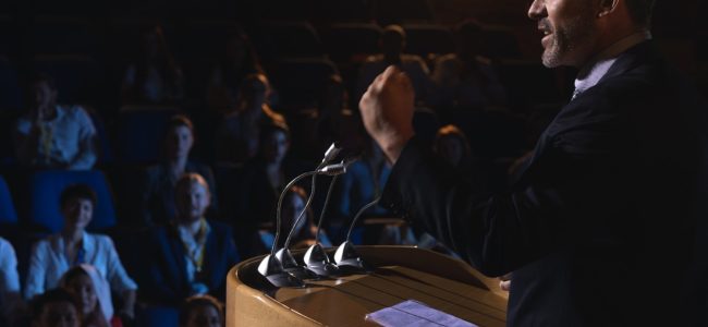 businessman-standing-giving-presentation-auditorium (1)